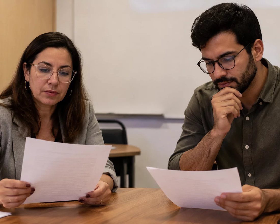 Dupla discute em pé entre as estantes de uma biblioteca, cada um sustentando o seu ponto